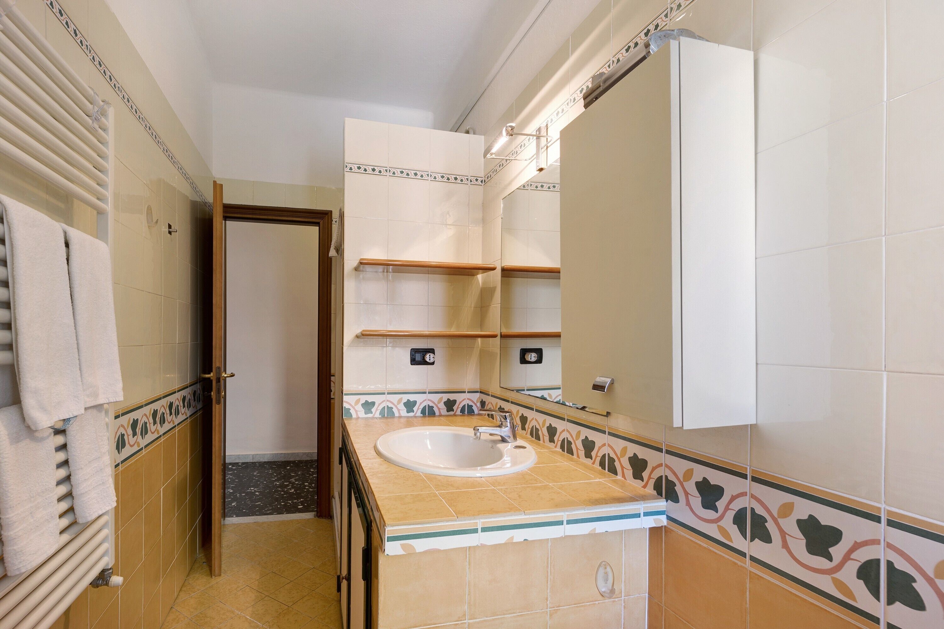 Une salle de bain équipée d’un lavabo, d’un miroir, d’un porte-serviettes et d’une porte donnant sur une autre pièce.