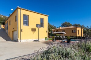 Un edificio amarillo con aro de baloncesto, zona de piscina y una escalera que lleva a un garaje.