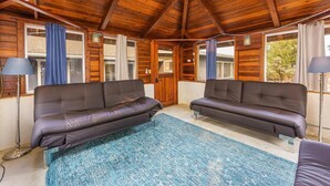 A cozy room with two leather sofas, a blue patterned rug, wooden ceiling beams, and large windows with curtains. - Lake View Hideaway Near Yosemite & Bass Lake (Oakhurst)