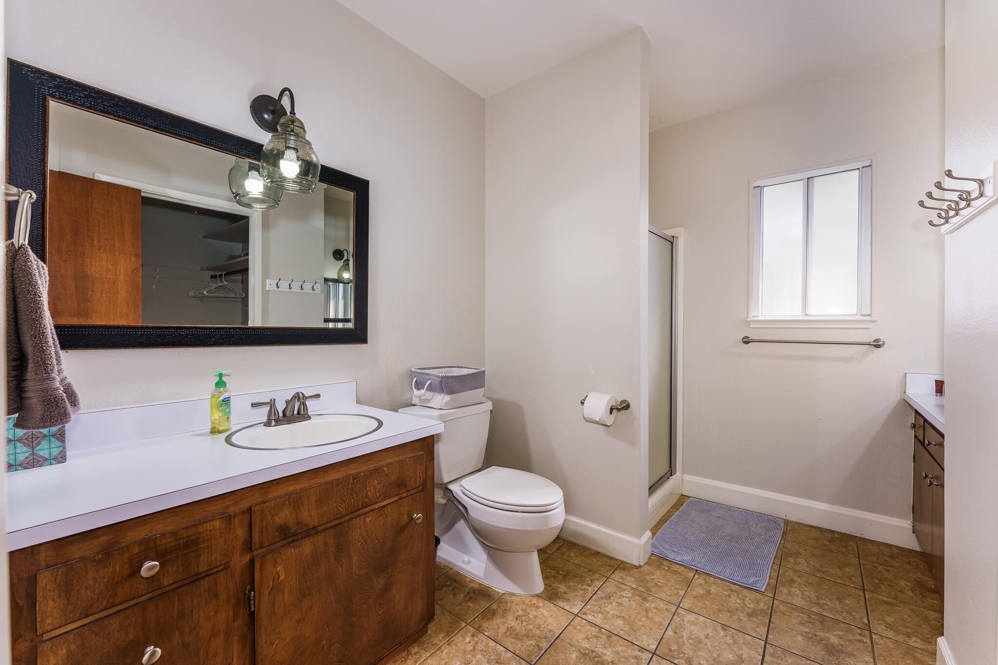 Un baño con lavamanos blanco, tocador de madera, inodoro, ducha y ventana.