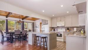 A modern kitchen with a central island, bar stools, and a dining area with a wooden table and chairs. - Lake View Hideaway Near Yosemite & Bass Lake (Oakhurst)