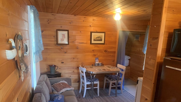 Un interior acogedor de cabaña con detalles de madera, una mesa de comedor con sillas, un sofá y un refrigerador.