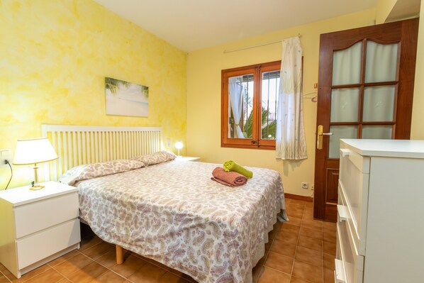 A bedroom with a bed, a nightstand, a lamp, a window with curtains, and a door. - Villa "Pelach" with Pool & Wi-Fi (Calonge)