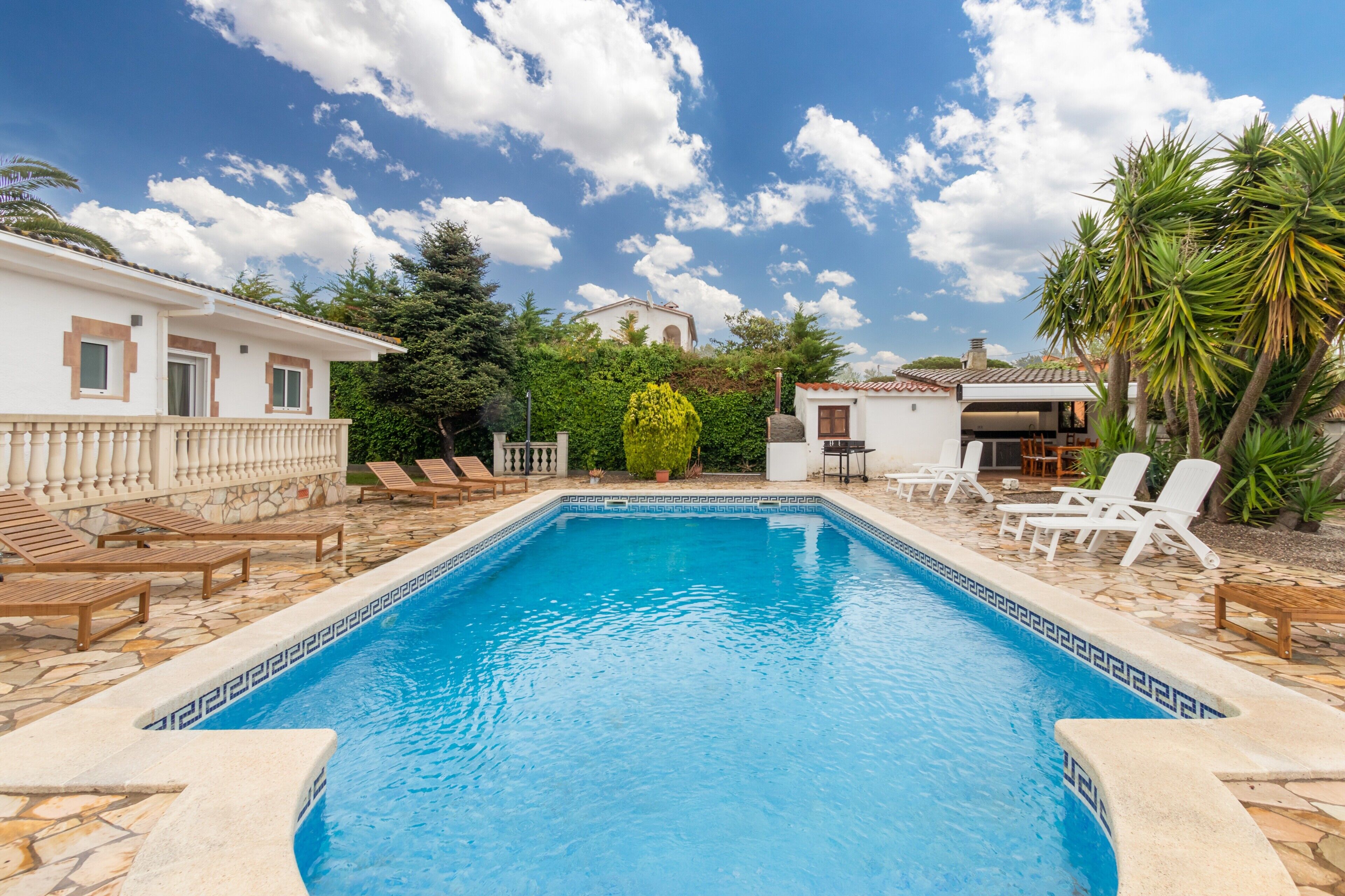 Una piscina con sillas de descanso, un edificio pequeño y una palmera.