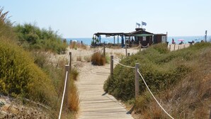 A wooden boardwalk leading to a beachside structure with flags, surrounded by vegetation.