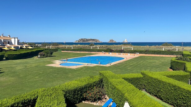 A swimming pool with a view of the sea, surrounded by well-maintained lawns and hedges.
