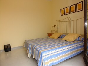 Un lit simple avec une couvre-lit à rayures, une table de chevet avec une lampe et un cadre photo fixé au mur.