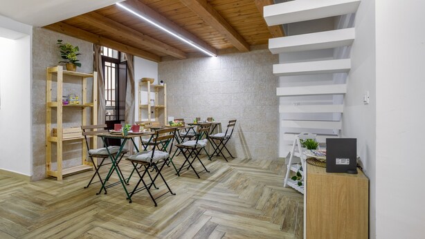 A dining area with wooden chairs and tables, a herringbone-patterned floor, a staircase, and a wall-mounted shelf with items.