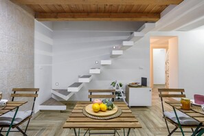 A modern interior with a wooden staircase, a dining area with a fruit centerpiece, and a white wall with a textured stone accent.