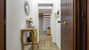 A hallway with a wooden door, a mirror, a small table with a vase, and a staircase in the background.