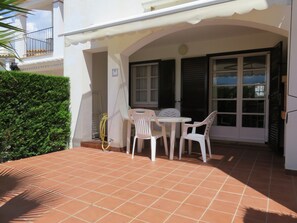 A patio with a tiled floor, a white table with two chairs, and a door with shutters.