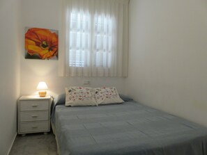 A bedroom with a bed, a nightstand, a lamp, a window with curtains, and a wall-mounted flower painting.