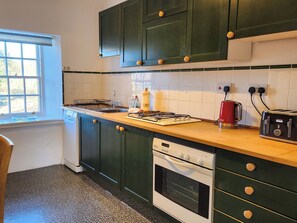 Una cocina con gabinetes verdes, una ventana, un fregadero, una estufa, un tostador y un lavavajillas.