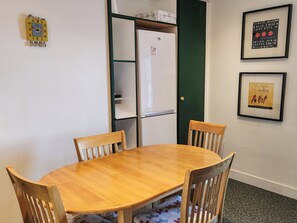Un coin repas avec une table en bois et quatre chaises, un réfrigérateur blanc et deux tableaux encadrés accrochés au mur.