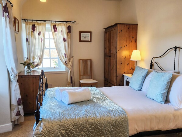 A bedroom with a bed, a wooden wardrobe, a chair, a bedside table with a lamp, and a window with curtains. - 2 bedroom accommodation in Cramond, Edinburgh (Cramond, Edinburgh)