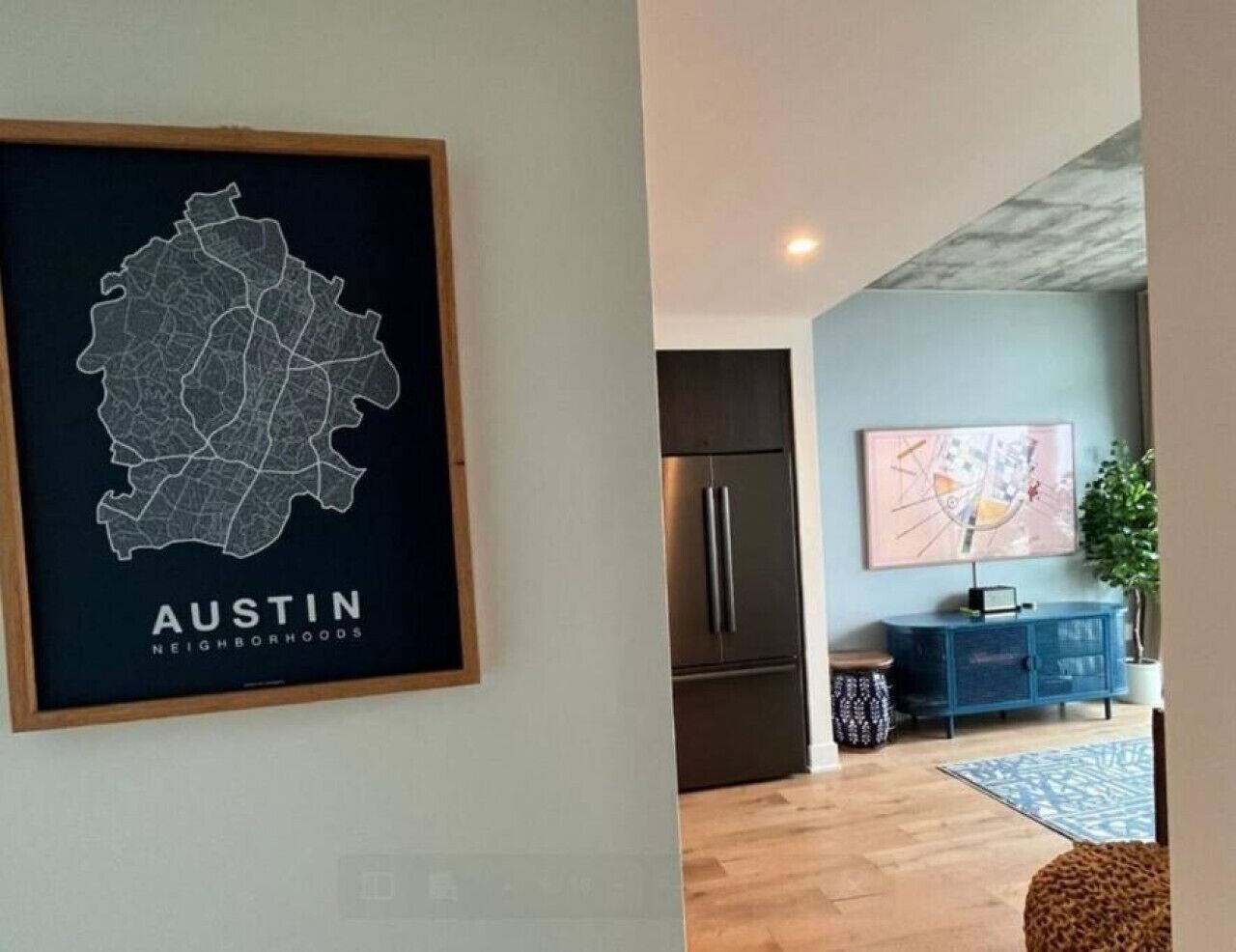 A framed map of Austin neighborhoods on a wall, a modern kitchen with a stainless steel refrigerator, and a blue cabinet with a plant.