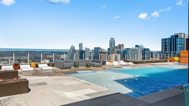 Ein Pool auf dem Dach mit Blick auf die Stadtlandschaft, eine Lounge mit Sitzgelegenheiten und einem klaren Himmel.