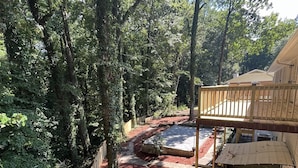 Eine überdachte Terrasse mit Holzgeländer, umgeben von dichtem Baumbestand und einem mit roter Rinde bedeckten Weg.