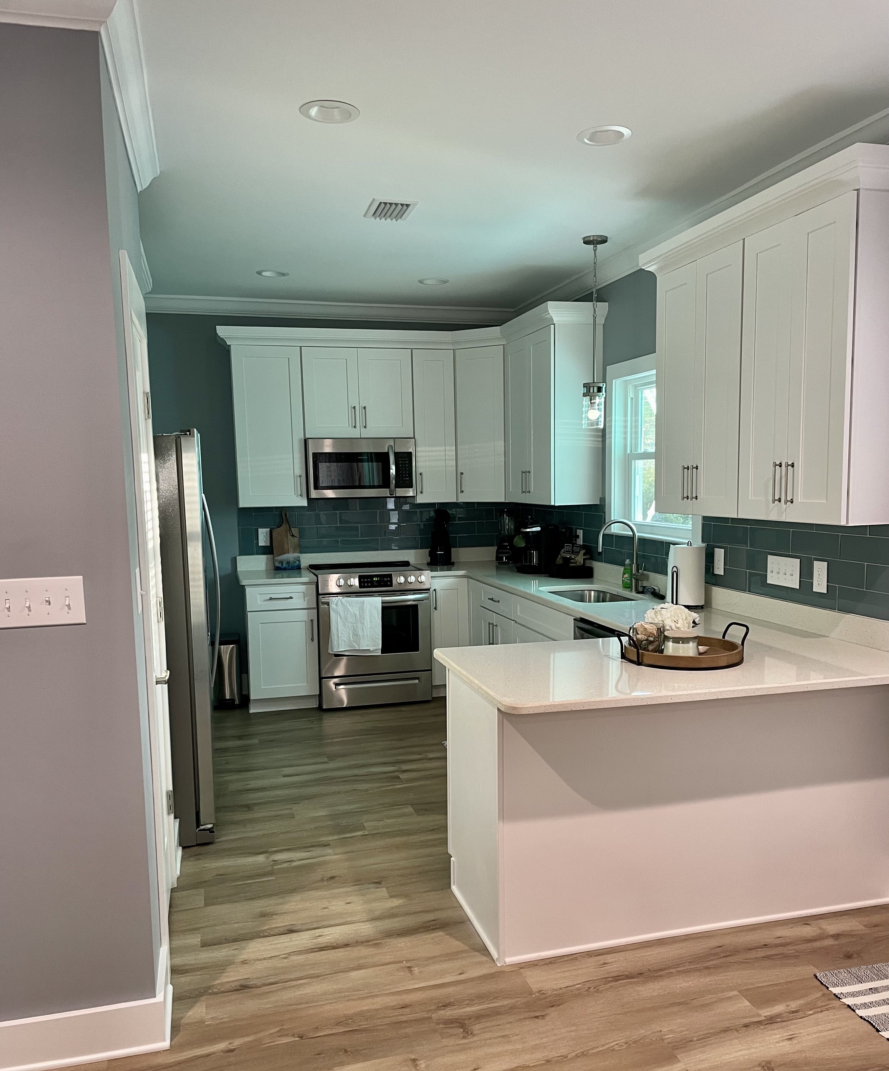 A modern kitchen with white cabinets, stainless steel appliances, and a wooden floor.