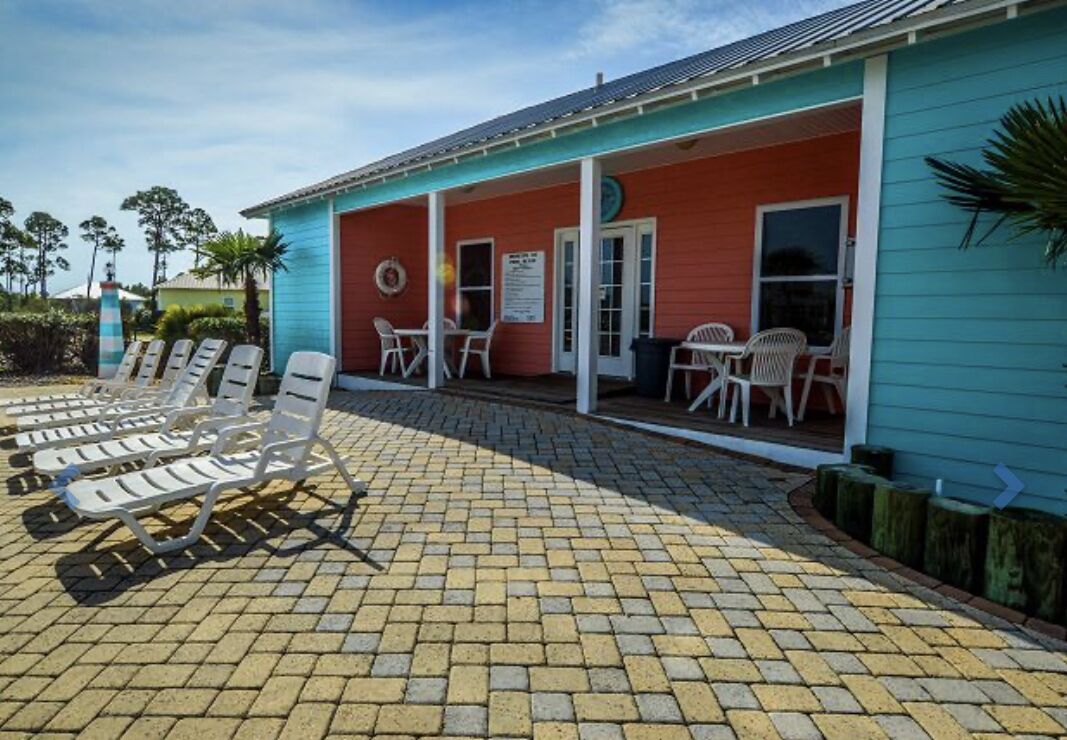 Un bâtiment à l’extérieur rouge, doté d’un patio couvert avec des chaises longues et des tables.