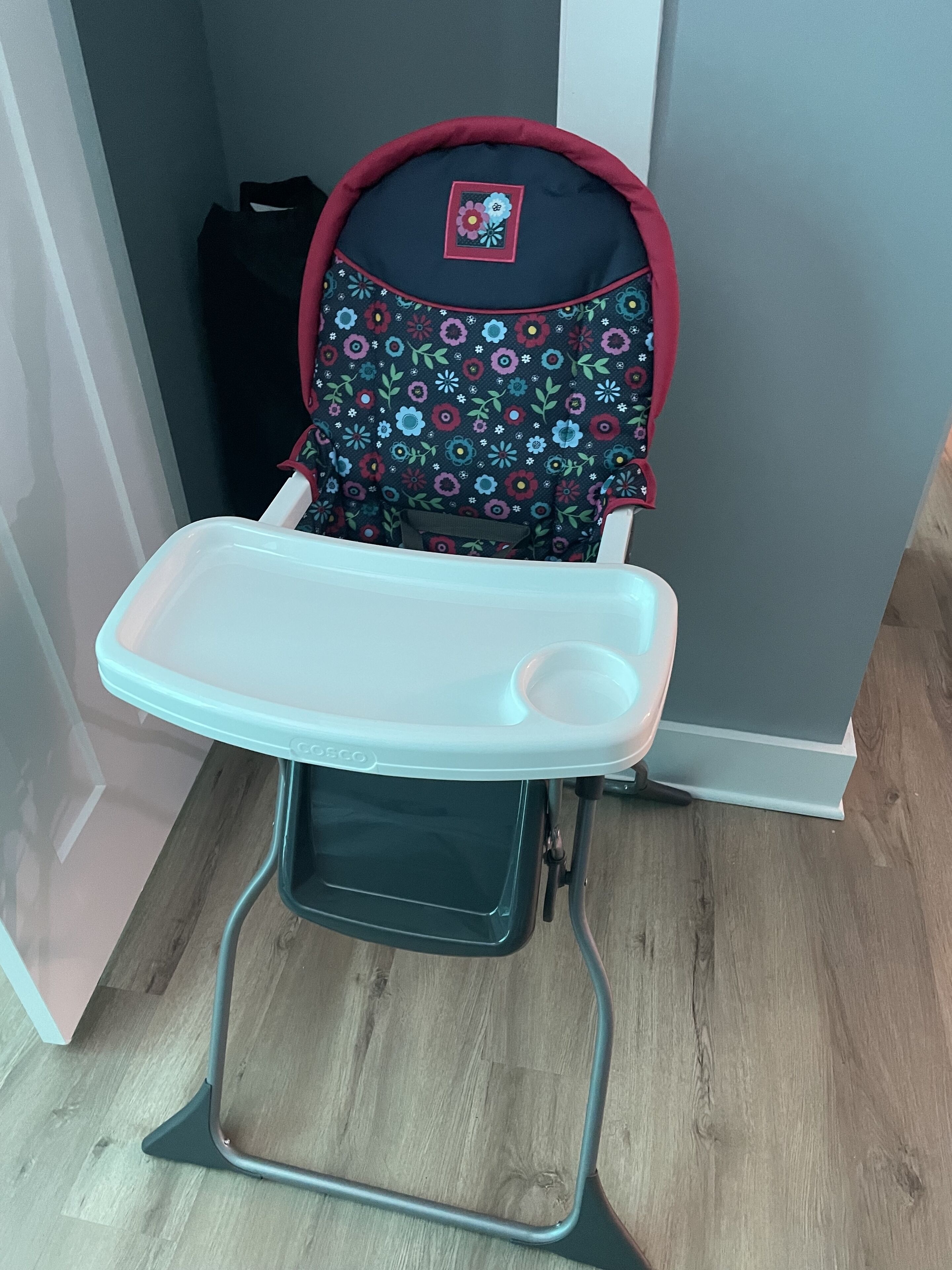 A high chair with a tray table, positioned in a room with wooden flooring and grey walls.