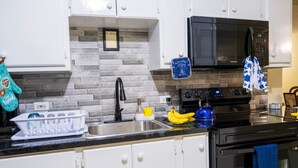 A kitchen with white cabinets, a black microwave, a stainless steel sink, and a blue kettle. - 3 Bedrooms in paradise w/fruit trees 3 mins-Oistins! (Oistins)
