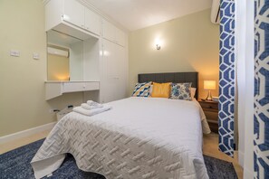 A neatly made bed with a white quilt, a bedside table with a lamp, a nightstand, and a large mirror above the bed. - 3 Bedrooms in paradise w/fruit trees 3 mins-Oistins! (Oistins)