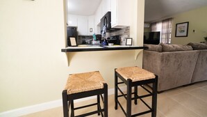 A modern kitchen with white cabinets, a black countertop, and two woven stools. - 3 Bedrooms in paradise w/fruit trees 3 mins-Oistins! (Oistins)