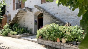 A stone building with a staircase leading to an entrance, surrounded by potted plants and greenery.