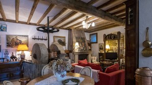 A rustic interior with exposed wooden beams, a stone fireplace, and a dining area with a table set for two.