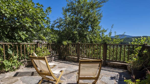 Two wooden chairs on a stone patio with a wooden fence and lush greenery in the background.