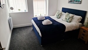 A neatly arranged bedroom with a bed, a bedside table, a nightstand, and a window with curtains.