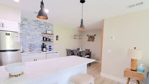 Una cocina moderna con una isla central, iluminación colgante y un comedor con mesa y sillas de madera.