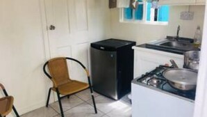 Eine kompakte Küche mit Gasherd, kleinem Kühlschrank und einem Fenster mit Vorhängen.