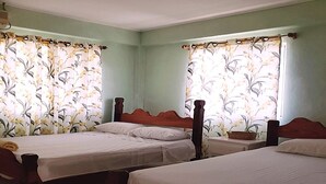 Ein Zimmer mit drei Einzelbetten, jeweils mit Holz Kopfteil und weißer Bettwäsche. Die Wände sind hellgrün gestrichen, und an den Fenstern hängen florale Vorhänge.