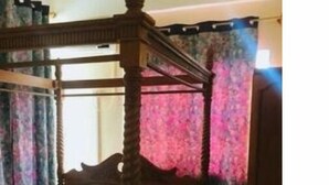 Ein Bett mit Baldachin, dessen Holzbettgestell einen weißen Überwurf und ein zusammengerolltes Handtuch trägt.