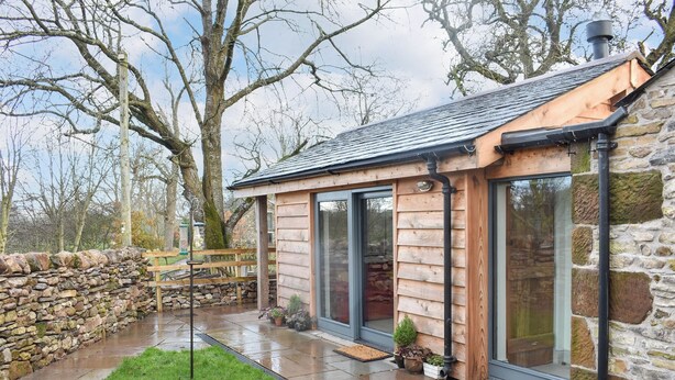 A log cabin with a stone wall, a wooden deck, and a stone staircase leading to a door.
