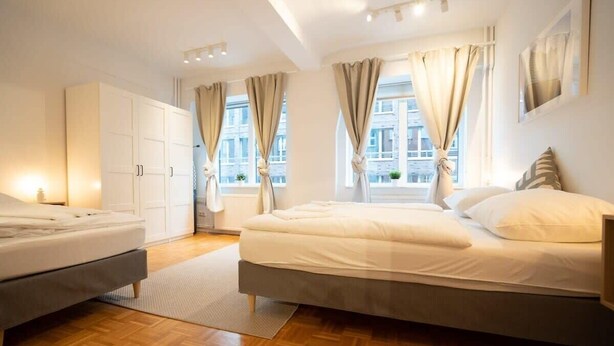 Un dormitorio moderno con una cama grande, una cama más pequeña, un armario y una ventana con cortinas.
