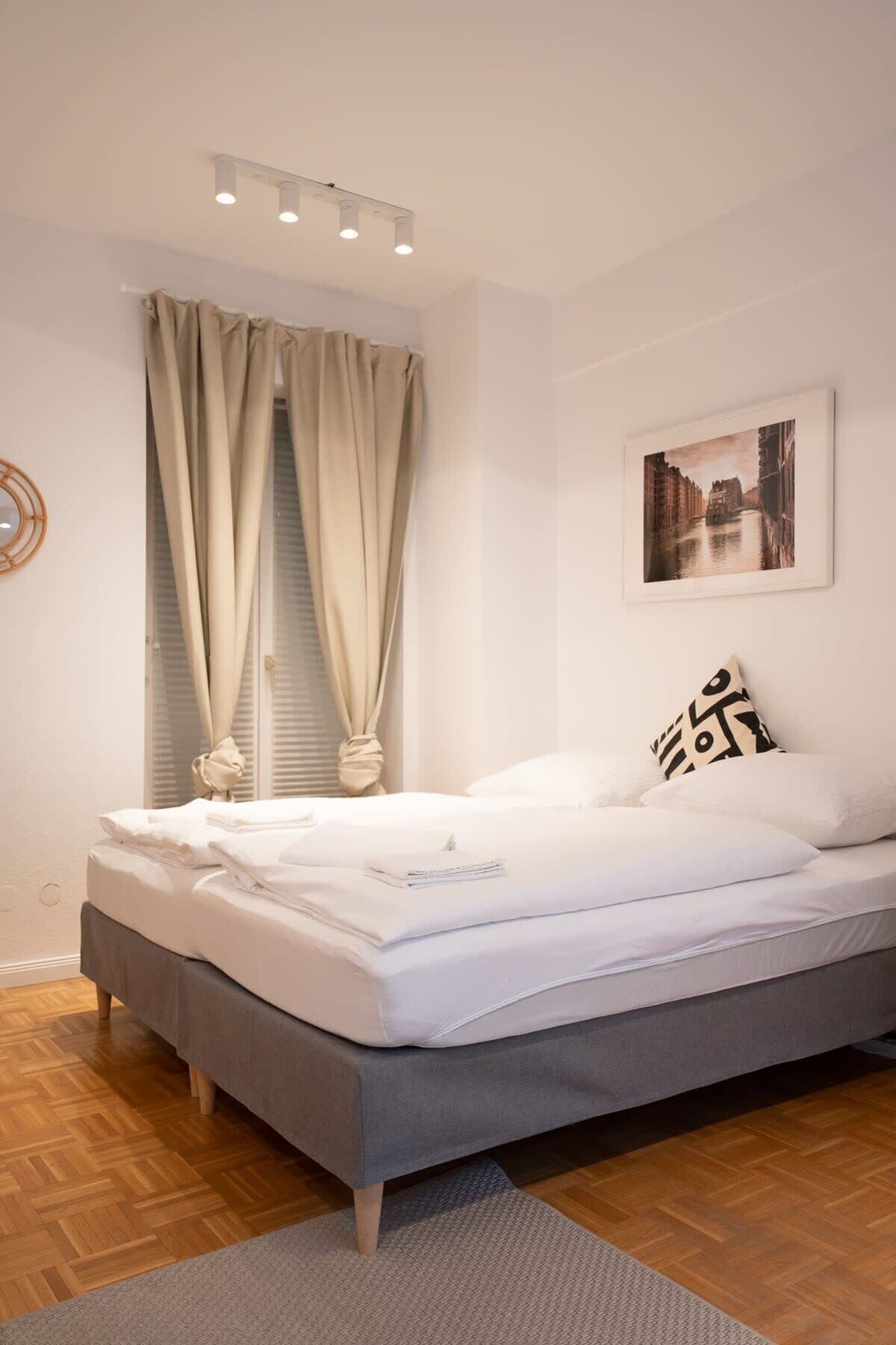 A neatly made bed with white linens, a grey headboard, and a single black and white pillow.