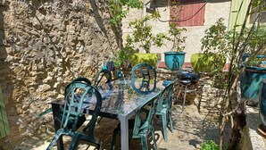 A patio with a glass table and green plastic chairs, surrounded by stone walls and potted plants.