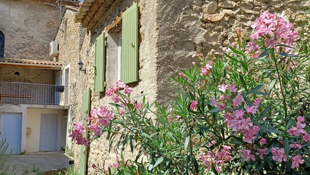 A rustic stone building with green shutters and a small balcony.