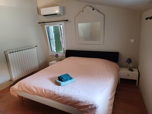 A bedroom with a bed, a nightstand, a lamp, a mirror, an air conditioner, and a window.