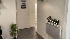 A hallway with a white door, a sign with multiple languages, a shelf with decorative items, and a vent with lights. - Studio 25 m² Côté Parc des Contades (Strasbourg)