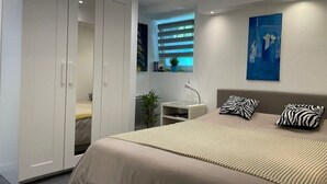 A modern bedroom with a large bed, a wardrobe, a bedside table, and a window with blinds. - Studio 25 m² Côté Parc des Contades (Strasbourg)