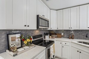 Une cuisine moderne avec des meubles blancs, une cuisinière noire et un four à micro-ondes placé au-dessus.