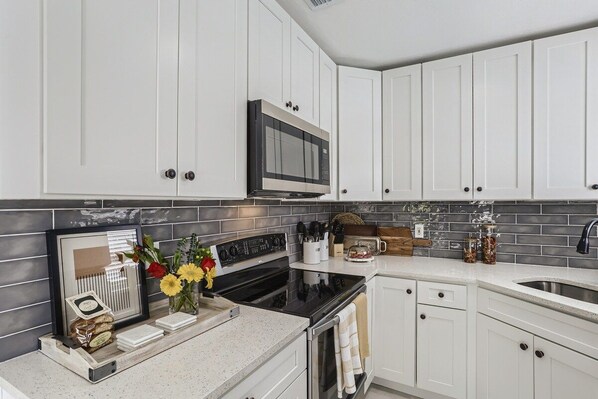 A modern kitchen with white cabinetry, a black stove, and a microwave above it.