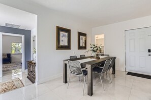 A dining area with a long table, six chairs, and two framed pictures on the wall.