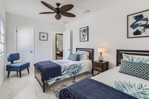 A bedroom with two beds, a ceiling fan, a chair, and artwork on the walls.