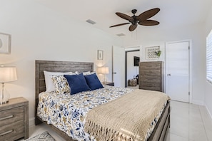 A bedroom with a bed, a ceiling fan, a nightstand, a dresser, and a door.