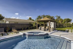 A backyard with a swimming pool, a covered patio, and a wooden fence.